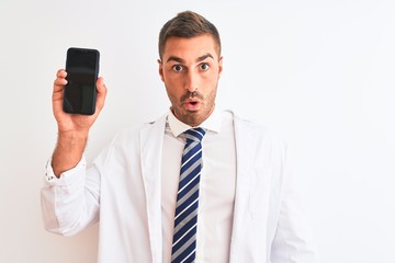 Naklejka premium Young scientist man showing smartphone screen over isolated background scared in shock with a surprise face, afraid and excited with fear expression