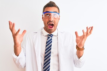 Young handsome scientist man wearing safety glasses over isolated background crazy and mad shouting and yelling with aggressive expression and arms raised. Frustration concept.