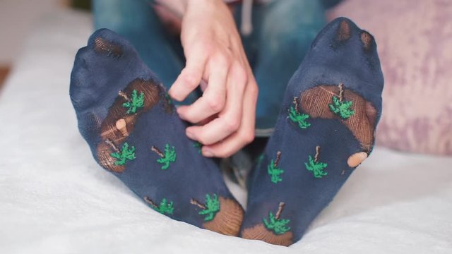 a man scratches his leg with his hands, on his feet are wearing holey socks