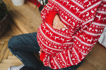 Top down belly of a pregnant woman wearing red ornamental christmas sweater