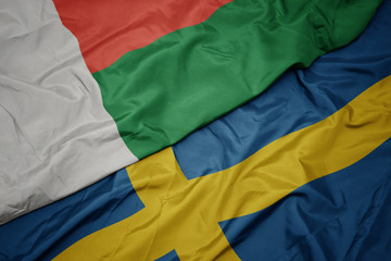 waving colorful flag of sweden and national flag of madagascar.