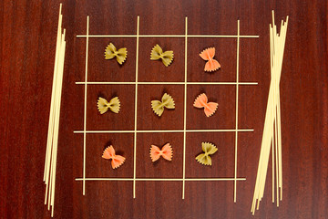 Italian pasta. Tic Tac Toe or Xs and Os game made from raw spaghetti, green and red farfalle. Dry...