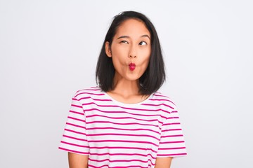 Young chinese woman wearing striped t-shirt standing over isolated white background making fish face with lips, crazy and comical gesture. Funny expression.