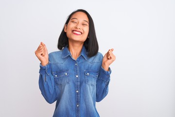 Young beautiful chinese woman wearing denim shirt standing over isolated white background excited...