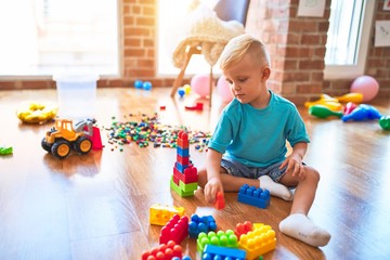 Young caucasian kid playing at kindergarten with toys. Preschooler boy happy at playroom.