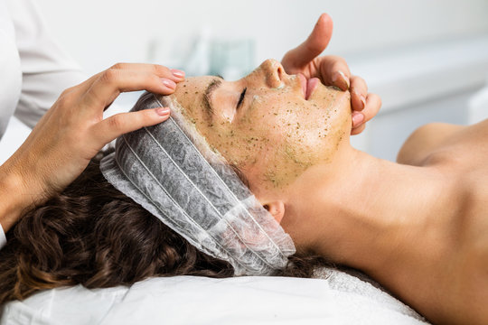 Beautiful woman receiving facial mask with rejuvenating effects in spa beauty salon.