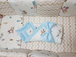 Beige bed linen in the baby cot. Textiles with a pattern of zigzags and bears. There are pillows,...
