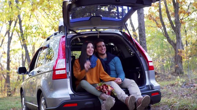 Young man and woman - romantic couple - are having fun, dancing and smiling in car trunk. Sunny autumn wood