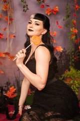 Slim fashion halloween girl with black hair in lace gothic pin up dress posing in the autumn background with fall leaves