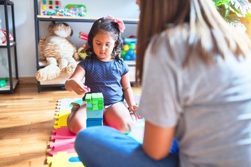Beautiful teacher and toddler girl playing with construction blocks bulding tower at kindergarten