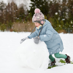 Adorable young girl building a snowman in the backyard. Cute child playing in a snow.