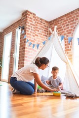 Beautiful teacher and toddler boy sitting on the floor playing inside  tipi at kindergarten