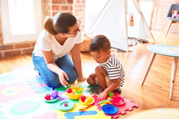 Beautiful toddler boy sitting on puzzle playing with plastic plates, fruits and vegetables at kindergarten