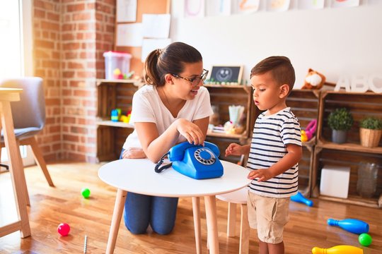 Beautiful teacher and toddler boy playing with vintage blue phone at kindergarten
