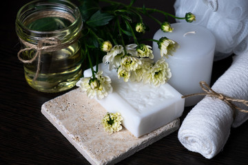 Handmade soap with a pattern lies on the table.  On a white table is handmade soap, flowers and olive oil.  Collection of items for the bathroom