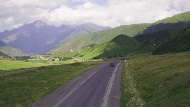 Black SUV driving alone on a beautiful road in the mountains at summer sunny day - Aerial drone view