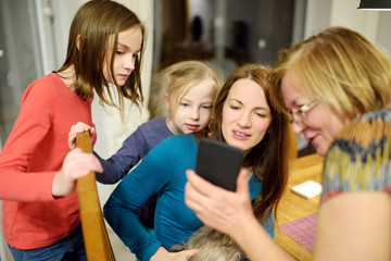 Beautiful family with young children using a smartphone and smiling while sitting by the table at home. Mom, grandma and kids making a call using a phone.