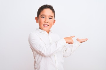 Beautiful kid boy wearing elegant shirt standing over isolated white background amazed and smiling to the camera while presenting with hand and pointing with finger.