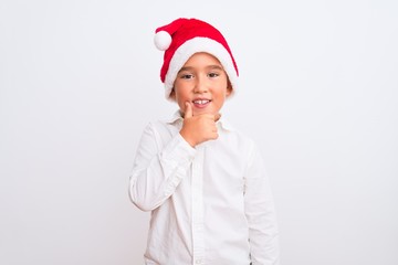 Beautiful kid boy wearing Christmas Santa hat standing over isolated white background looking confident at the camera with smile with crossed arms and hand raised on chin. Thinking positive.