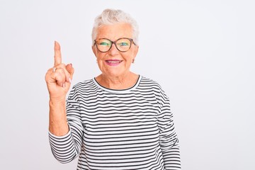 Senior grey-haired woman wearing striped navy t-shirt glasses over isolated white background showing and pointing up with finger number one while smiling confident and happy.