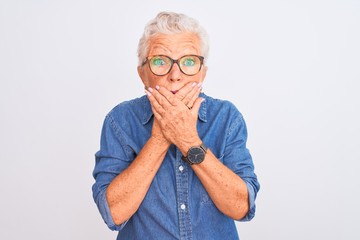 Senior grey-haired woman wearing denim shirt and glasses over isolated white background shocked covering mouth with hands for mistake. Secret concept.