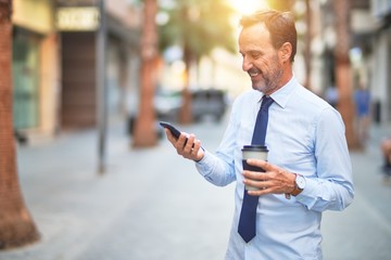 Middle age handsome businessman using smartphone drinking take away coffee smiling
