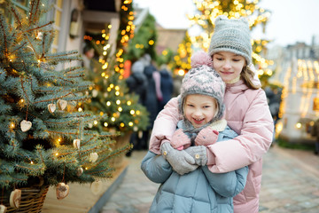 Two adorable sisters having a good time together on traditional Christmas fair in Riga, Latvia. Children enjoying sweets, candies and gingerbread on Xmas market.