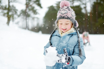 Fototapeta na wymiar Adorable young girl having fun in beautiful winter park. Cute child playing in a snow. Winter activities for family with kids.