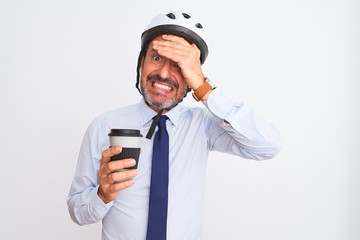 Middle age businessman wearing bike helmet drinking coffee over isolated white background stressed with hand on head, shocked with shame and surprise face, angry and frustrated. Fear and upset