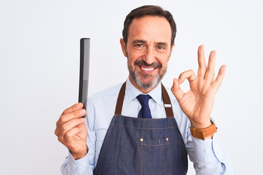 Middle age barber man wearing apron holding hair comb over isolated white background doing ok sign with fingers, excellent symbol