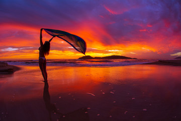Woman on the beach at sunrise holding a silk sarong in the wind
