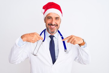 Middle age doctor man wearing christmas hat and stethoscope over isolated white background looking confident with smile on face, pointing oneself with fingers proud and happy.
