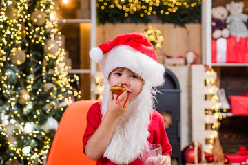 Portrait of little Santa child holding chocolate cookie and glass of milk. Santa Claus takes a cookie on Christmas Eve as a thank you gift for leaving presents.
