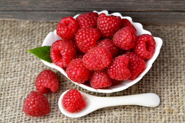 Freshly picked raspberries in a white bowl on a burlap cloth background.Healthy food concept.Selective focus.