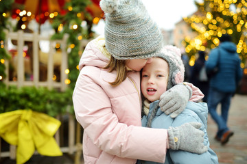 Obraz premium Two adorable sisters having a good time together on traditional Christmas fair in Riga, Latvia. Children enjoying sweets, candies and gingerbread on Xmas market.