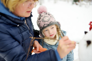 Cute little girl and her grandma building a snowman in the backyard. Cute child playing in a snow.
