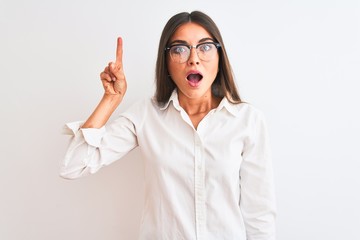 Young beautiful businesswoman wearing glasses standing over isolated white background pointing finger up with successful idea. Exited and happy. Number one.
