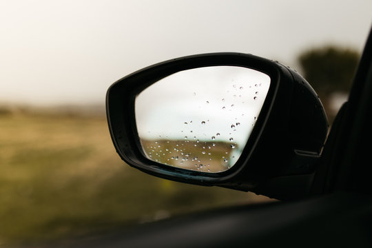 Rear view mirror seen through the glass. Wet car window. Close up rain drop. Car view see the mirror.