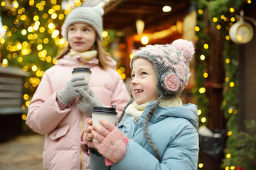 Two adorable sisters drinking hot chocolate on traditional Christmas fair in Riga, Latvia. Children...