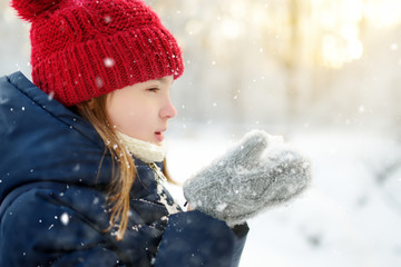 Adorable young girl having fun in beautiful winter park. Cute child playing in a snow. Winter activities for family with kids.