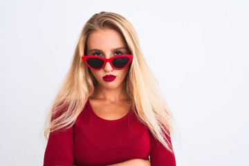 Young beautiful woman wearing red t-shirt and sunglasses over isolated white background skeptic and nervous, disapproving expression on face with crossed arms. Negative person.