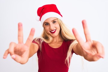 Young beautiful woman wearing Christmas Santa hat over isolated white background smiling looking to the camera showing fingers doing victory sign. Number two.