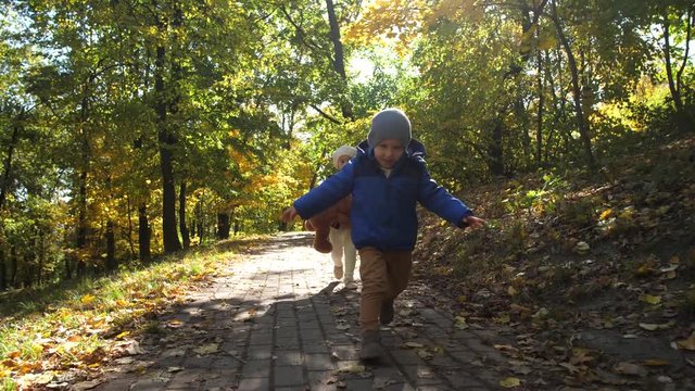 Happy toddler brother and his older sister with down syndrome enjoying play while running along park path on sunny autumn day. Joyful little kids flying while running during joint outdoor leisure