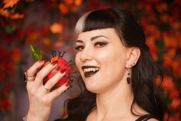 beautiful halloween girl in black pin up clothes with dead red apple in the hand on autumn leaves background alone