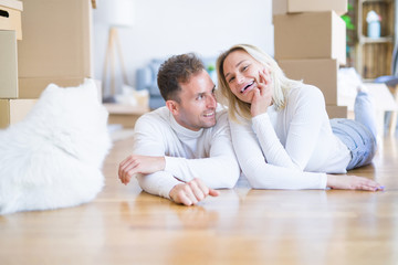 Obraz premium Young beautiful couple with dog lying down on the floor at new home around cardboard boxes