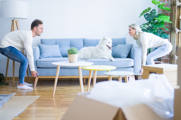 Young beautiful couple with animal moving sofa at new home around cardboard boxes