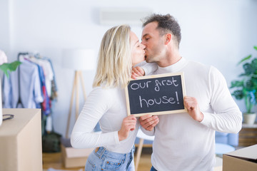 Fototapeta na wymiar Young beautiful couple standing holding blackboard with message kissing at new home around cardboard boxes