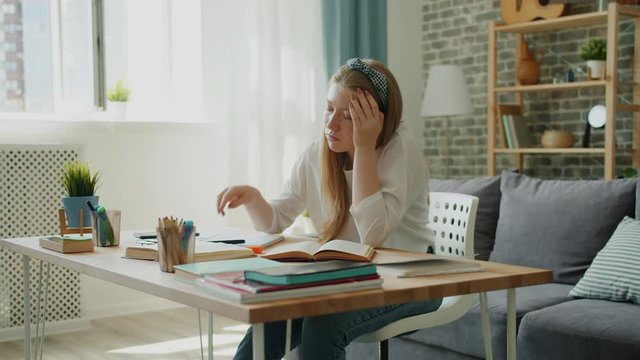 Tired young girl is doing homework at home then sleeping on desk feeling exhausted preparing for exams. Teenage health, lifestyle and education concept.