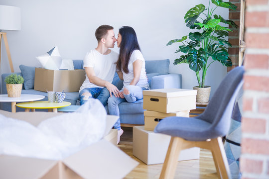 Young beautiful couple sitting on the sofa drinking coffee at new home around cardboard boxes