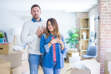 Young beautiful couple standing at new home around cardboard boxes smiling with hands on chest with closed eyes and grateful gesture on face. Health concept.